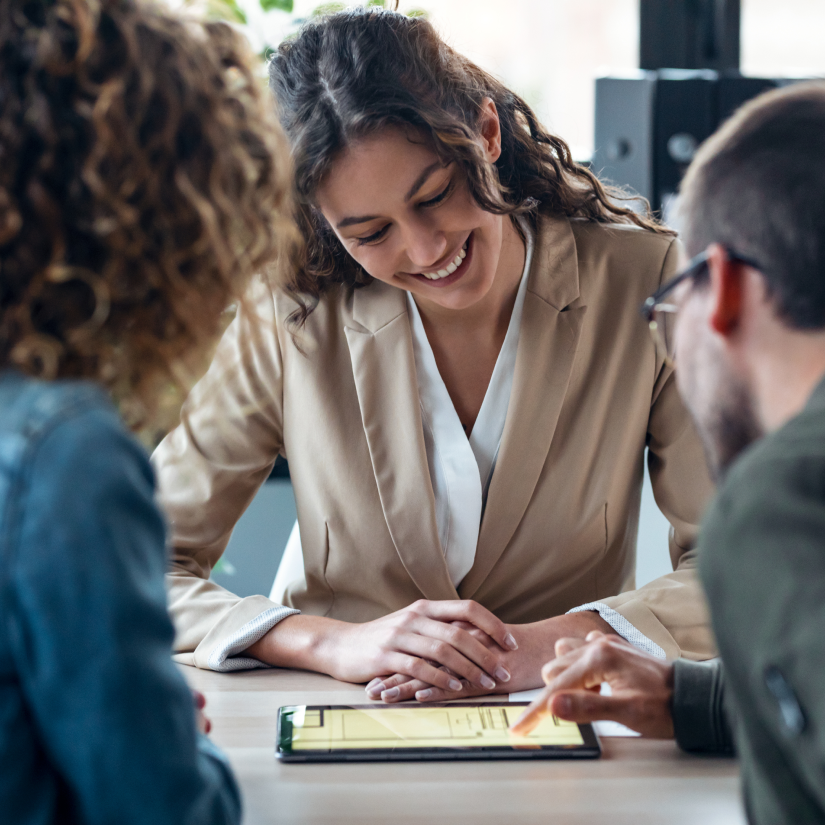 Female professional showing digital documents on an iPad to a happy couple